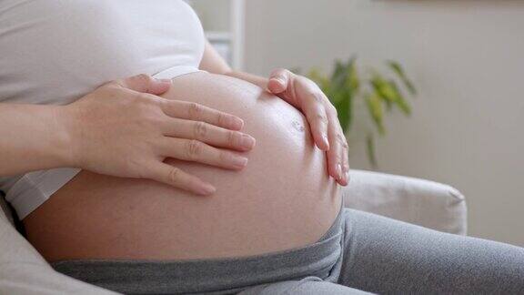 年轻的亚洲孕妇手爱抚腹部坐在沙发上在家里怀孕产妇准备和预期