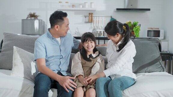 亚洲家庭坐在一起微笑看着相机的肖像在家里爸爸、妈妈和小女儿互相看着开心地笑着家庭活动