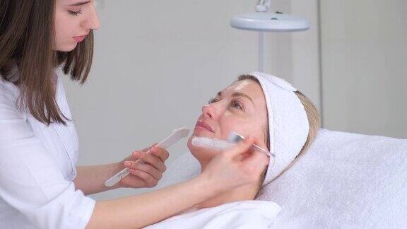 在美容院用粘土面膜护理一位女士的脸美容和水疗