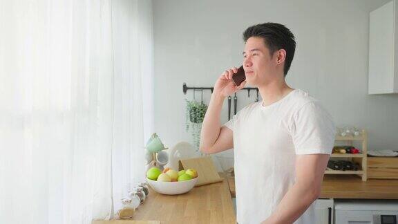 亚洲帅哥站在家里厨房里打电话快乐有魅力的男性早上站在窗外享受假日周末用智能手机与科技交流