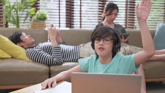 开朗的亚洲男孩在线课程学习从家里亚洲男孩举手回答来自在线老师的问题亚洲男孩和爸爸妈妈坐在家里的生活区学习笔记本电脑
