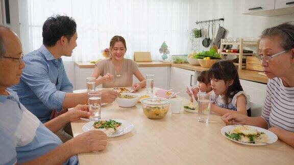 亚洲大家庭在家里的餐桌上共进午餐年长的祖父母年轻的夫妇和年幼的孩子女儿感到幸福享受在家里吃的食物活动关系