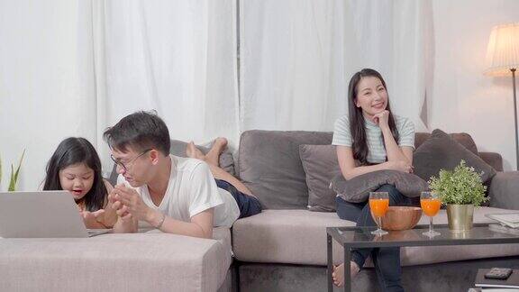 快乐的亚洲家庭在客厅妈妈在看电视女儿和爸爸在用笔记本电脑