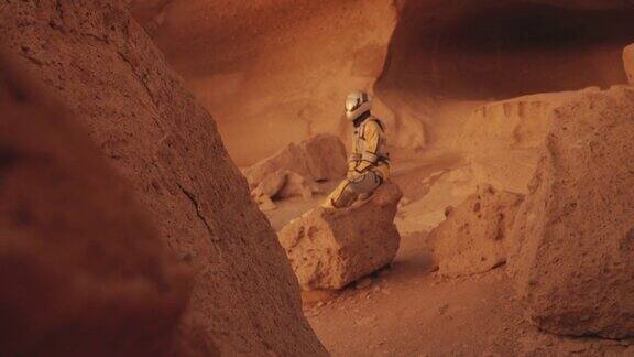 在火星上的孤独探索铁锈色洞穴和岩石的女宇航员坐在岩石上