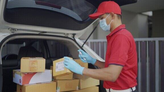 4k慢动作视频一名穿着红色制服的男性快递员寄包裹盒子在村里的汽车后备箱里喷洒清洁酒精新标准