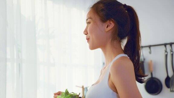 亚洲有吸引力的运动妇女拿着沙拉碗和吃蔬菜美丽的运动女孩穿着运动服享受吃干净的蔬菜后在家里的健康饮食和健康食品