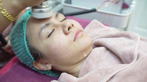 一名护士使用超声波机在一名亚洲妇女的脸上按摩在美容诊所医疗和美容皮肤科预约概念