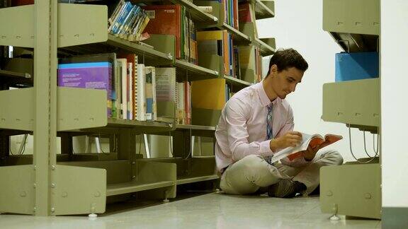 一个白人老师正坐在图书馆的地板上看书