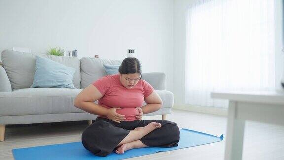 亚洲健美女性在客厅里做瑜伽锻炼运动女孩坐在自由地板上伸展手根据在线教练的指导为健康减肥