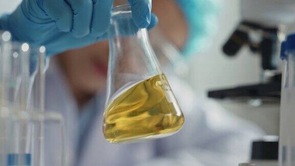 科学家戴着手套手持装有黄色液体的无菌烧瓶