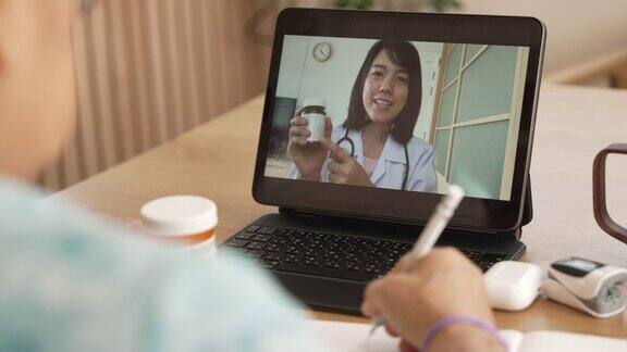 高级亚洲妇女在与医生在线咨询期间做笔记