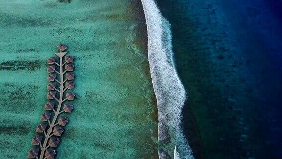 鸟瞰热带岛屿度假酒店的平房和绿松石般的印度洋海浪在马尔代夫从上面看豪华的水房间和冲浪海浪冲