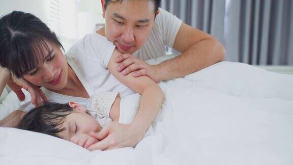 慈爱的亚洲父母在家里照顾熟睡的女儿漂亮幸福的家庭夫妇早上爸爸妈妈把毯子盖在睡着的小宝宝的床上
