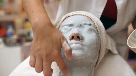 年轻的亚洲女性在水疗中心用维他命面膜按摩脸部