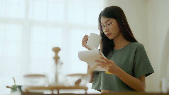 快乐的年轻亚洲女人戴着眼镜在厨房在家里女专心读书笔记做饭