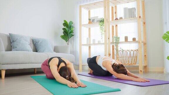 亚洲活跃的女性朋友在家里一起做瑜伽普拉提锻炼漂亮的女孩穿着运动服用垫子在家里的客厅里利用空闲时间进行保健健身