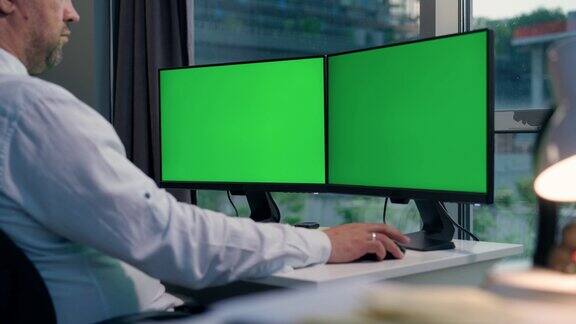一名男子使用带有两个绿屏模型的台式电脑在家工作