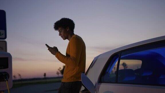 黄昏时分一个年轻人在停车场给他的电动汽车充电