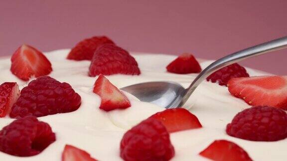 用勺子舀酸奶和覆盆子和草莓绕圈旋转酸奶与浆果在粉红色的背景