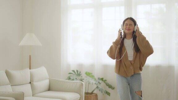 年轻的亚洲女性戴着耳机在家里客厅的地板上跳舞快乐亚洲女性微笑放松在家里健康的心理健康和幸福