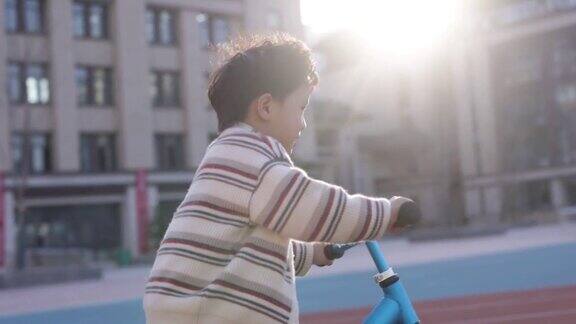 这个小男孩正在学校操场上骑自行车