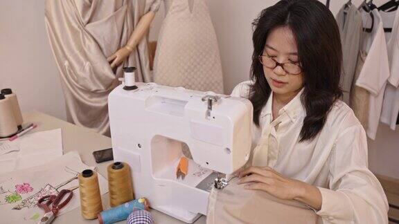 亚洲服装设计师正在使用电动机器缝制衣服的4k视频片段在办公室在家里专业手工业概念小型企业
