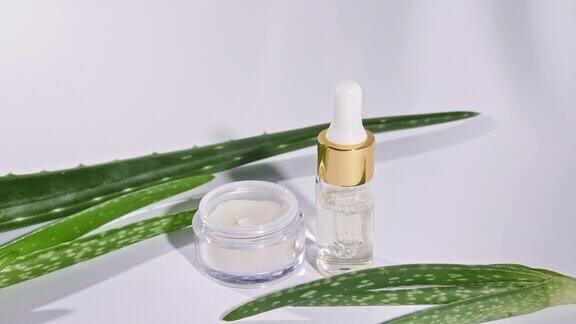 滴管玻璃瓶与天然化妆品油芦荟白色面霜瓶皮肤和身体护理热带棕榈叶的运动与阴影在白色的背景