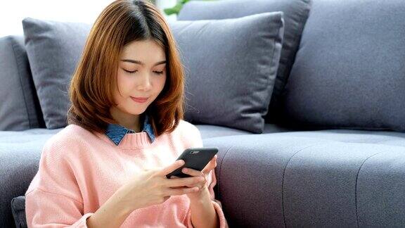 年轻美丽的亚洲女人使用智能手机与幸福坐在沙发上人们在电话生活方式