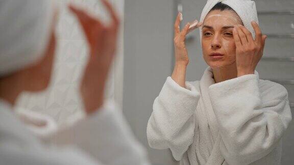 女士使用保湿泡沫洗脸和微笑早上的护肤程序年轻的女学生头上缠着毛巾在水疗沙龙照镜子准备化妆