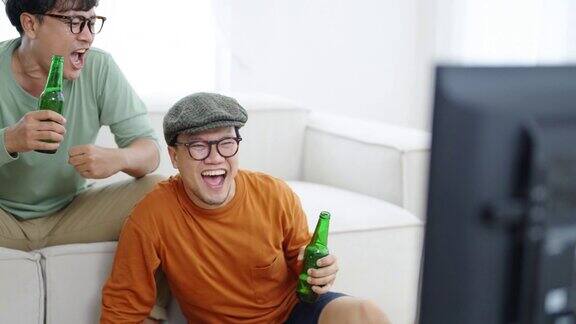 4K亚洲男子朋友一起在家里看电视上的体育比赛