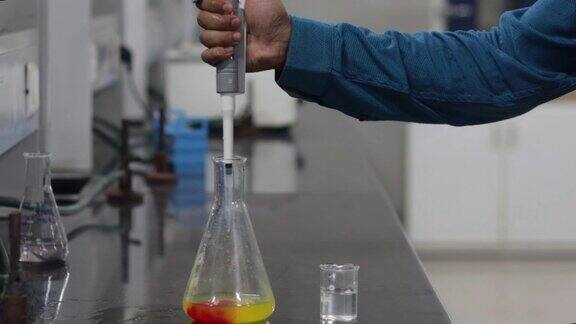 一名研究科学家的双手将一种无色的化学物质从微型吸管倒入一种黄色的化学物质在锥形瓶中造成红色