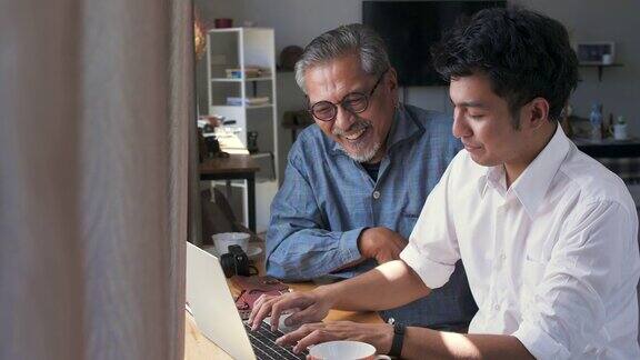 亚洲老父亲和他成年的儿子坐在家里使用笔记本电脑