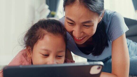 亚洲蹒跚学步的小女孩女儿和妈妈在地毯地板上玩数码平板电脑玩得开心在家里的客厅里快乐