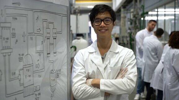 一个快乐的亚洲学生站在实验室的白板旁边对着镜头微笑双臂交叉
