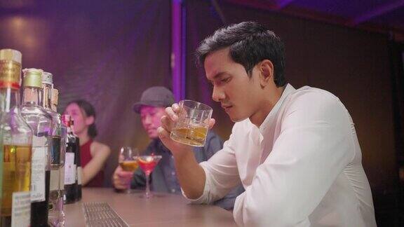 亚洲抑郁男子感到心碎在酒吧喝啤酒迷人的男性坐在吧台拿着一瓶酒感到孤独醉醺醺的宿醉独自在夜店