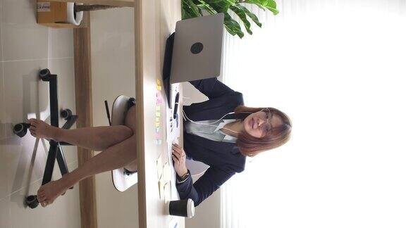 亚洲女商人套装和短裤坐在沙发上使用笔记本电脑在她的客厅商务会议