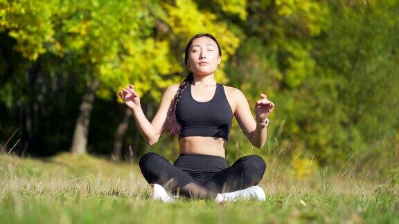 年轻美丽的运动女孩亚洲女子在公园冥想坐莲花姿势练习瑜伽垫禅在户外自然放松在早晨健康的生活理念