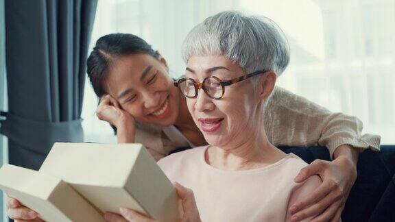 快乐的亚洲女儿惊喜礼物生日礼物在红色礼盒退休资深母亲坐在沙发沙发在家里