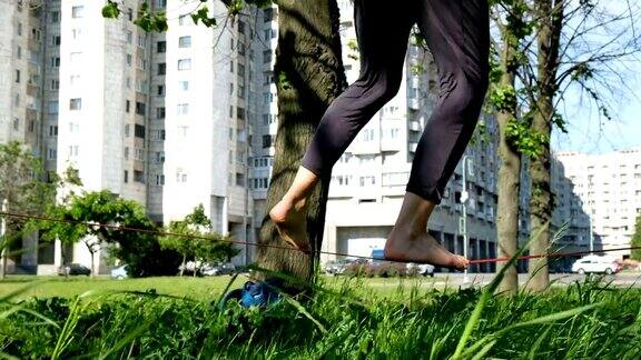 一个欧洲女孩在城市公园里走钢丝女人在松紧带上保持平衡特写