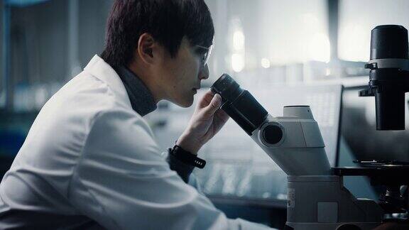 医学发展实验室:东亚科学家在显微镜下观察的肖像分析培养皿样本大型制药实验室做医学生物技术微生物学药物研究