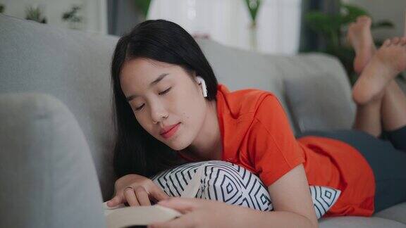 快乐的年轻亚洲女性躺在沙发上用智能手机听音乐