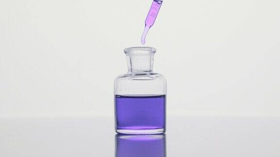 滴管将紫色油滴入灰色背景的试剂瓶中