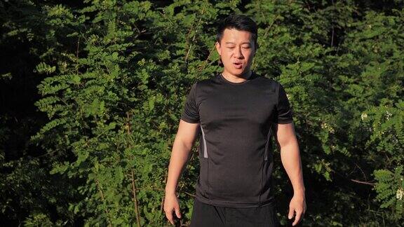 正面积极健康的年轻韩国男子做深蹲锻炼在街道日落背景的绿色树木夏季男性户外锻炼运动运动健康