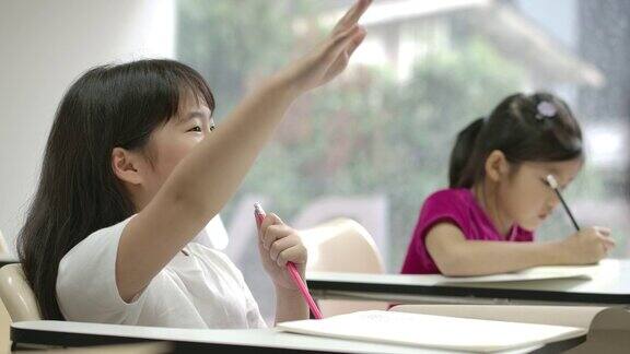 一个亚洲小女孩在教室里举起手臂回答老师的问题幼儿园学前概念