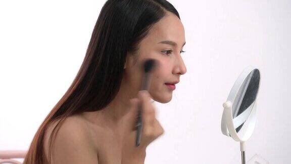 亚洲女性喜欢自己化妆年轻迷人的美丽感到快乐的看着镜子和着色眉毛在脸上享受美丽的化妆在白色的背景