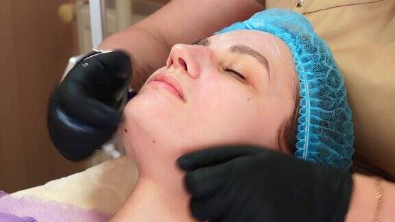 特写化妆师在医疗手套使用均匀的化妆品霜或防晒霜后脱皮女性的脸护肤和防晒美容院美容