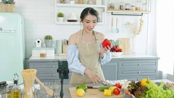 亚洲女性美食博主在智能手机摄像头前烹饪沙拉同时在家里的厨房里录制视频和直播