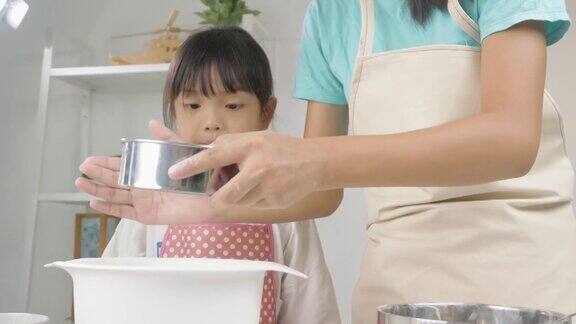 快乐的亚洲孩子在家里学习做饼干女孩筛面粉到搅拌碗