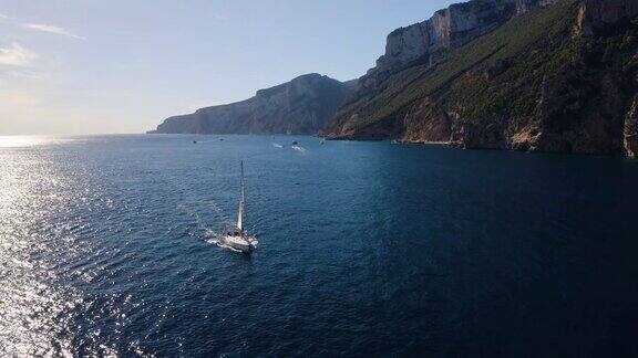 夏季日落时帆船在蓝色海面上的鸟瞰图去意大利撒丁岛旅游热带海景有帆船、海湾、高山、绿树、海洋、天空无人机俯瞰游艇游艇