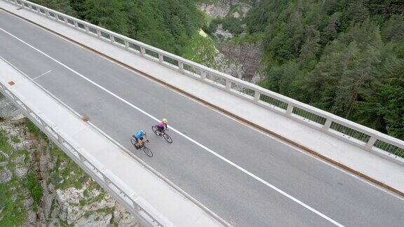 两名公路自行车手在高山峡谷上方的一座桥上骑行
